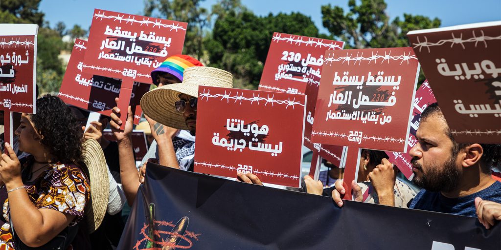 LGBTQI+ rights protesters from the Damj advocacy group hold signs stating “Our identity is not a crime” and “Down with the shameful article, a vestige of colonialism!” June 2024 in Tunis. (Photo courtesy of Nawaat/Alaa Agreb)i