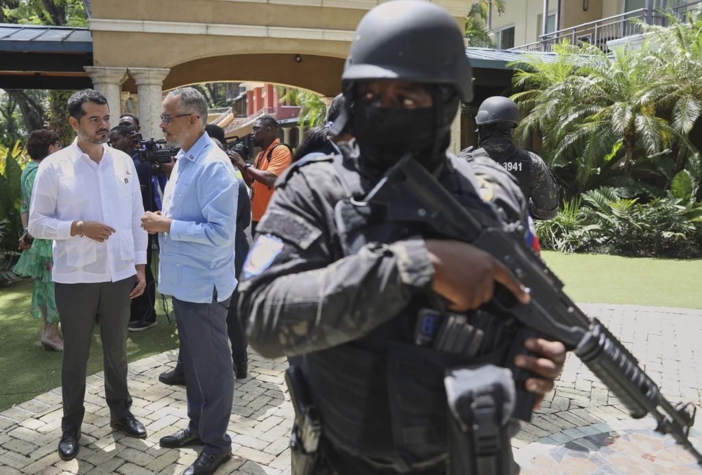 Armed security guard protects Haiti's acting prime minister, Alix Didier Fils-Aime, center, after an event in July that marked one year since a severely outgunned Multinational Security Support Mission began trying to restore order in the capital city. (Odelyn Joseph photo courtesy of AP and NPR)